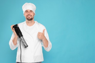 Smiling chef holding sous vide cooker and showing thumb up on light blue background