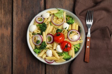Bowl of delicious pasta with tomatoes, onion and broccoli on wooden table, top view