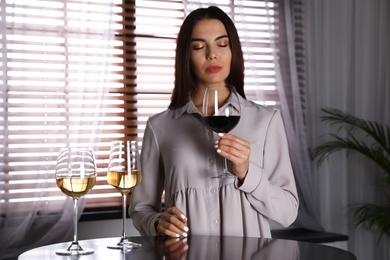 Photo of Beautiful young woman tasting luxury wine at table indoors