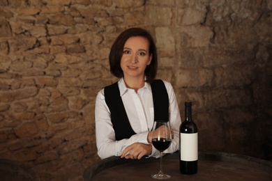 Female sommelier with glass and bottle of red wine at table indoors