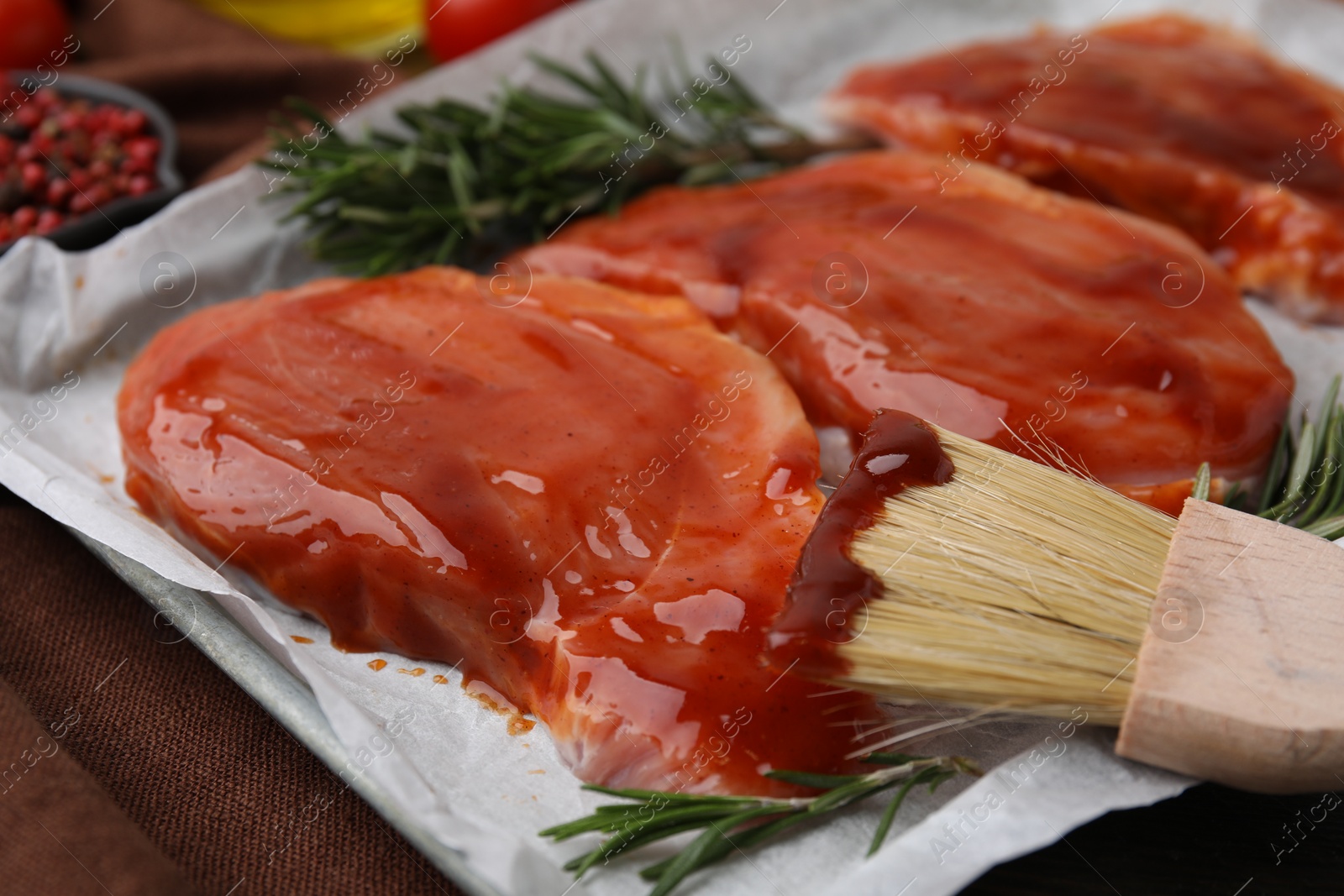 Photo of Raw marinated meat, rosemary and basting brush on table, closeup