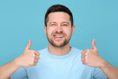 Happy man showing his tongue and thumbs up on light blue background
