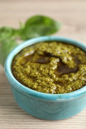 Photo of Tasty pesto sauce in bowl and basil on wooden table, closeup