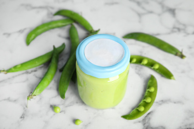 Baby food in jar and fresh green peas on white marble table