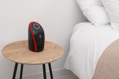Photo of Modern compact electric heater on coffee table near bed indoors