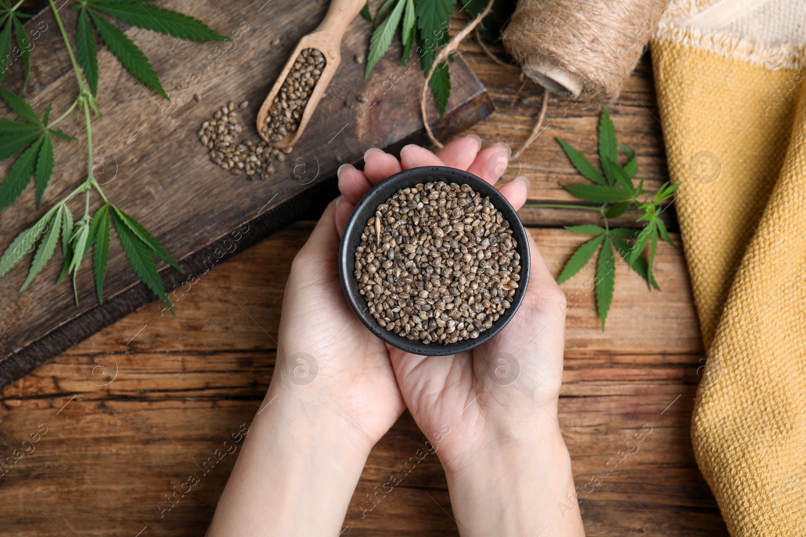 Photo of Woman holding bowl of organic hemp seeds at wooden table, top view