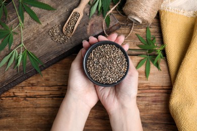 Woman holding bowl of organic hemp seeds at wooden table, top view