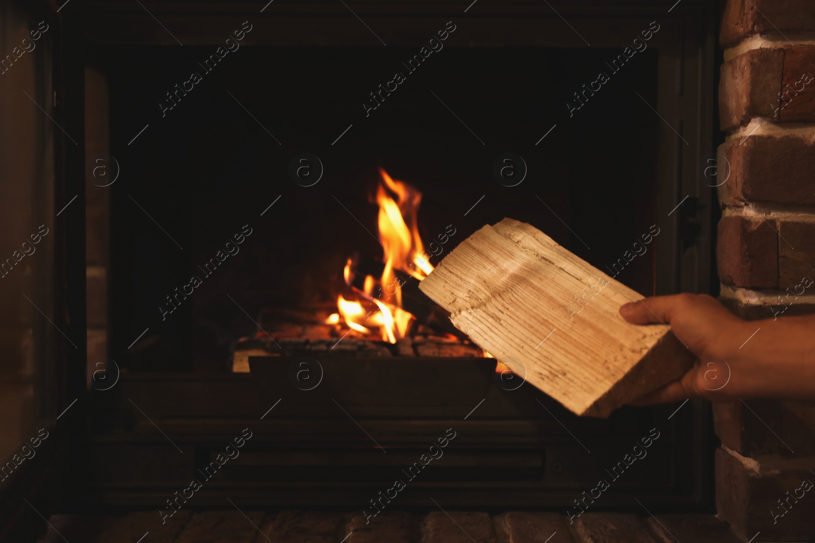 Photo of Man putting dry firewood into fireplace at home, closeup. Winter vacation