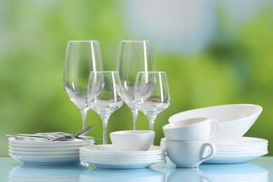 Photo of Set of many clean dishware, cutlery and glasses on light blue table against blurred green background
