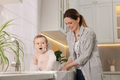 Mother washing her little baby in sink at home