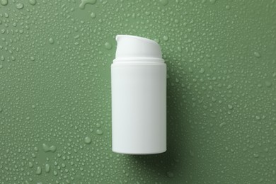 Photo of Moisturizing cream in bottle on green background with water drops, top view