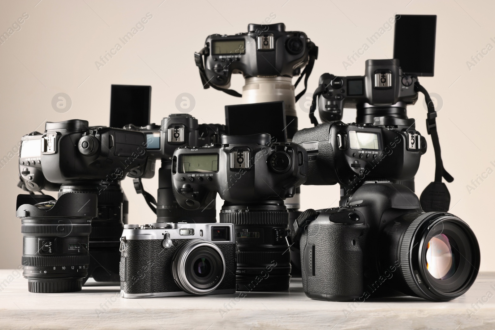 Photo of Modern cameras on white wooden table against light background