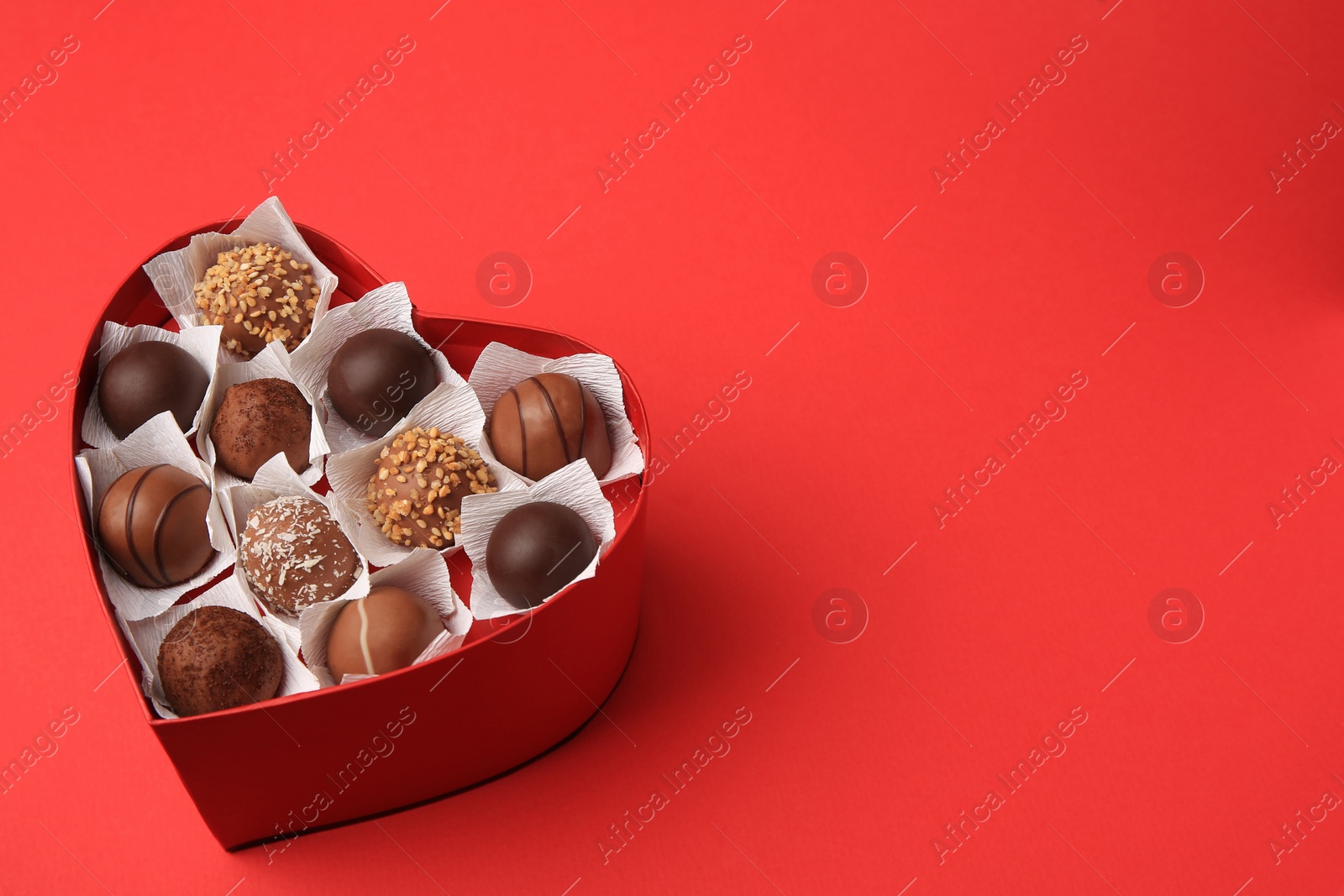 Photo of Heart shaped box with delicious chocolate candies on red table. Space for text