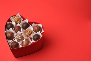 Heart shaped box with delicious chocolate candies on red table. Space for text