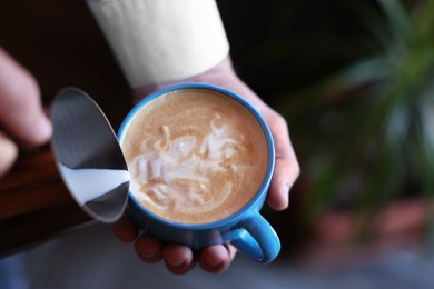Photo of Barista pouring milk into cup of coffee on blurred background, closeup. Space for text