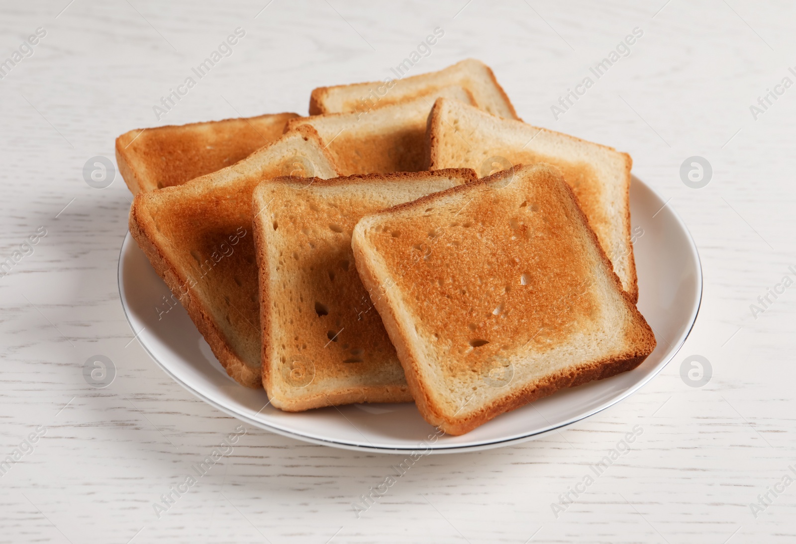 Photo of Plate with slices of delicious toasted bread on white wooden table