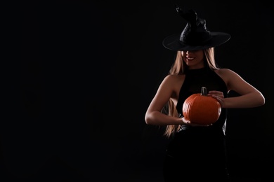 Photo of Young woman wearing witch costume with pumpkin on black background, space for text. Halloween party