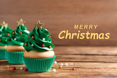 Image of Greeting card with phrase Merry Christmas. Festively decorated cupcakes on wooden table