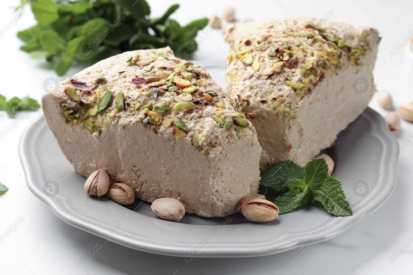 Photo of Pieces of tasty halva with pistachios and mint on white table, closeup