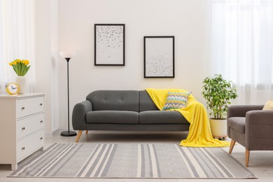 Photo of Spring atmosphere. Stylish living room interior with comfortable furniture and bouquet of beautiful yellow tulips