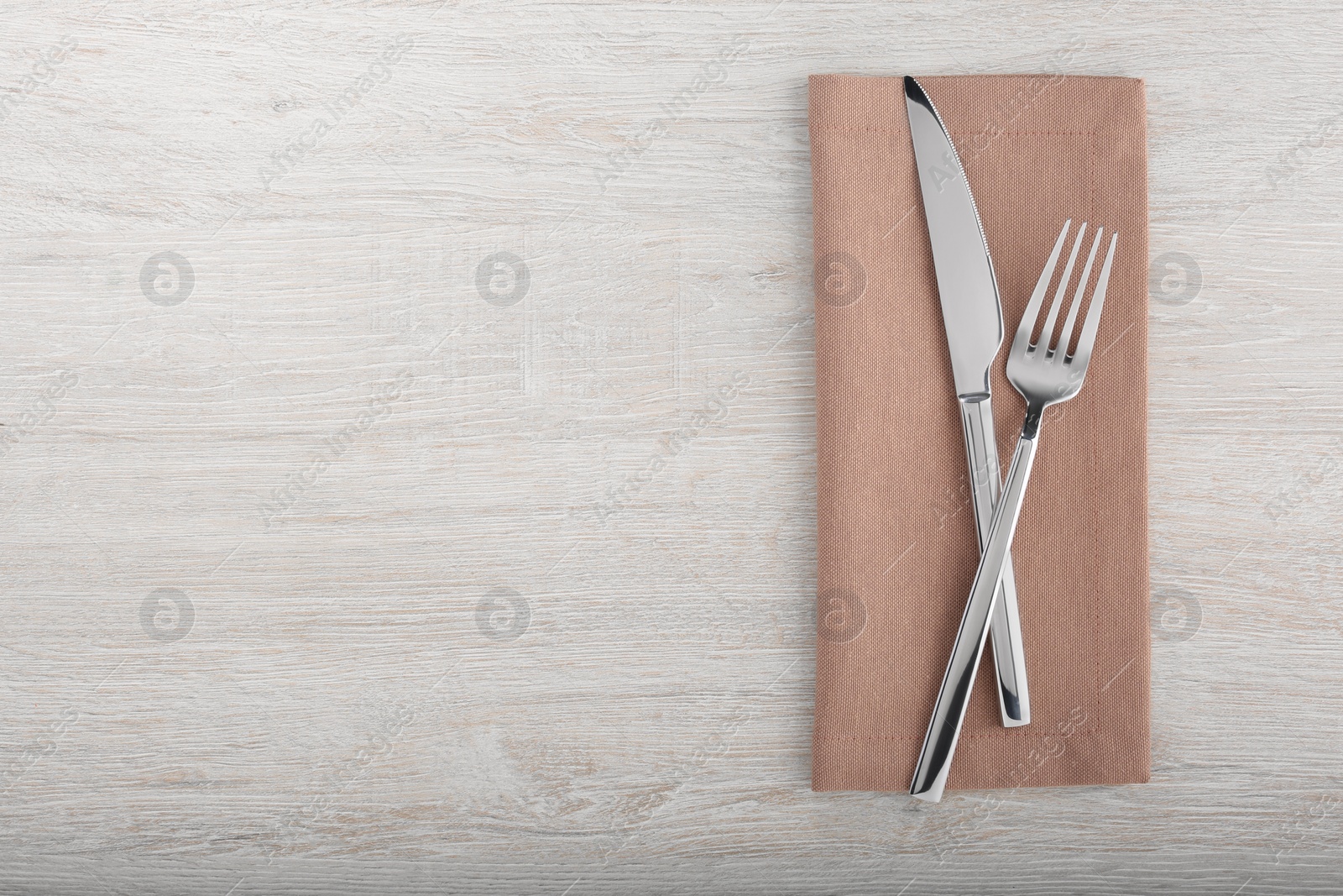 Photo of Shiny fork, knife and napkin on white wooden table, flat lay. Space for text