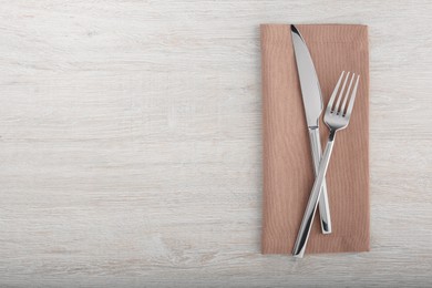 Photo of Shiny fork, knife and napkin on white wooden table, flat lay. Space for text