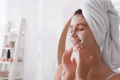 Photo of Beautiful teenage girl applying cleansing foam onto face in bathroom, space for text. Skin care cosmetic