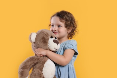 Photo of Cute little girl with teddy bear on orange background