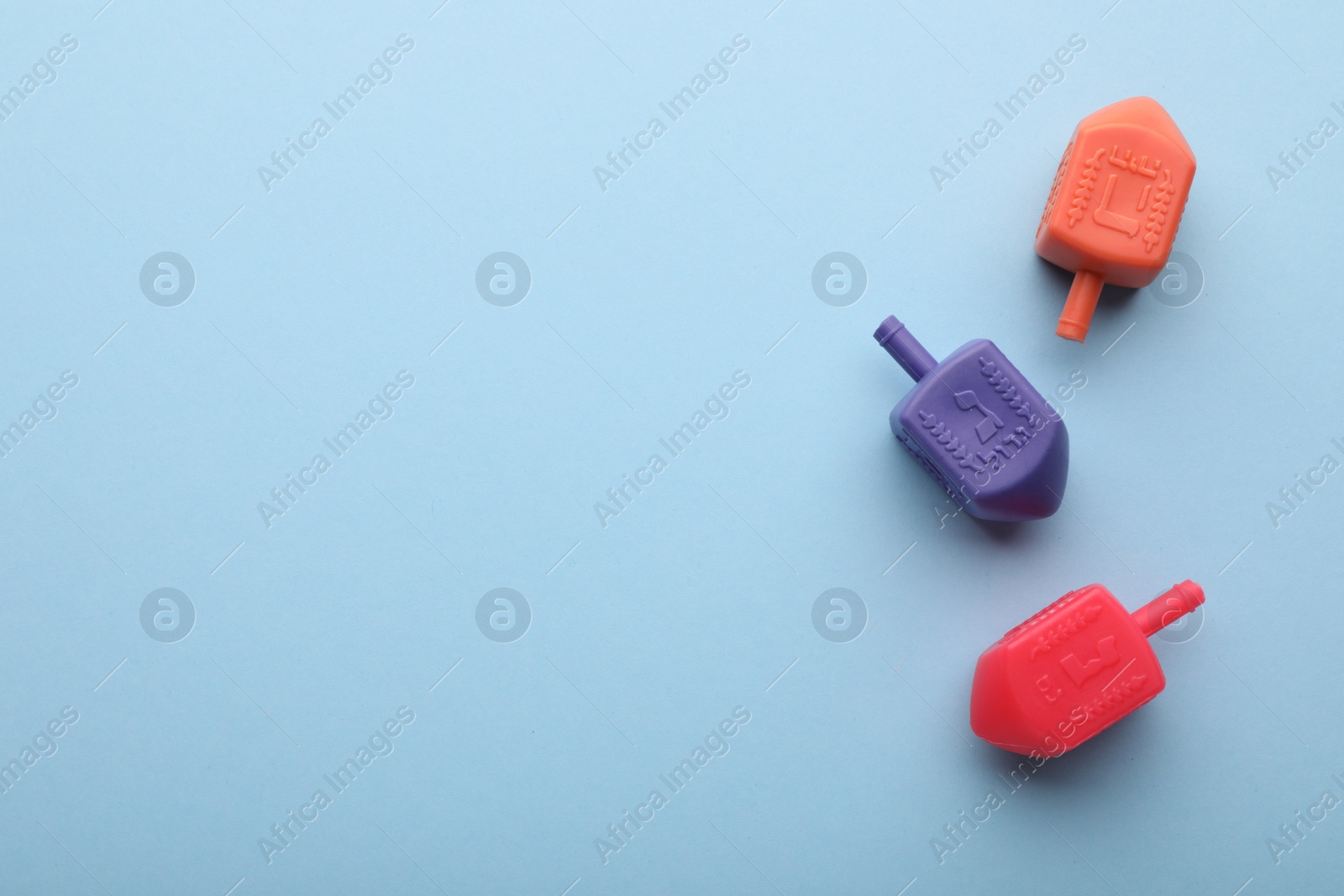 Photo of Colorful dreidels on light blue background, flat lay with space for text. Traditional Hanukkah game