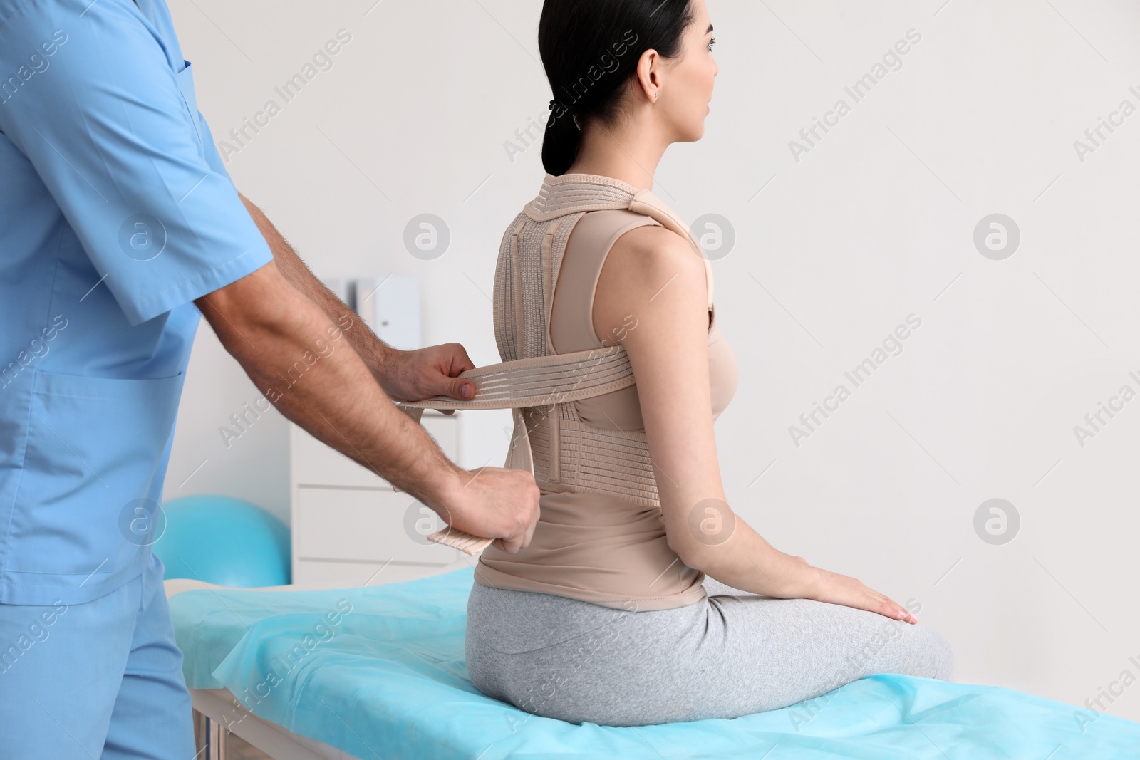 Photo of Orthopedist helping patient to put on posture corrector in clinic, closeup. Scoliosis treatment