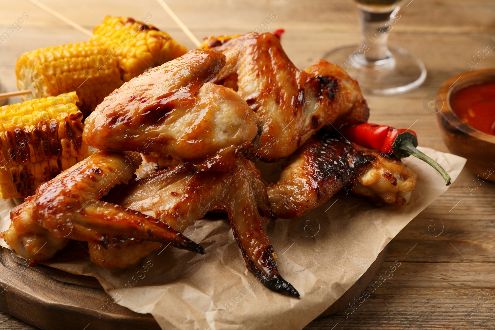 Photo of Delicious baked chicken wings and grilled corn served on wooden table, closeup