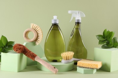 Bottles of cleaning product, sponge and brushes on light green background