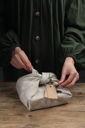 Photo of Furoshiki technique. Woman wrapping gift in fabric at wooden table, closeup