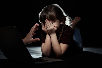 Photo of Stranger reaching frightened little child with laptop on dark background. Cyber danger