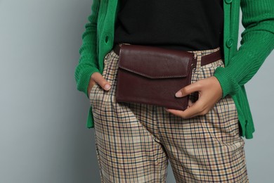 Young African American woman with stylish waist bag on grey background, closeup