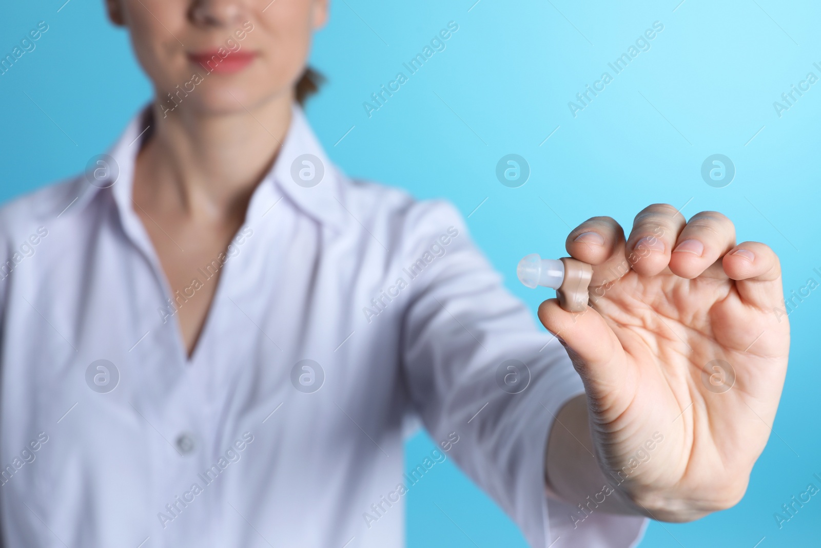 Photo of Female doctor holding hearing aid on color background, closeup. Medical object