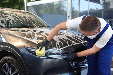 Young worker cleaning automobile with sponge at car wash