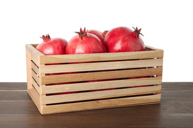 Fresh pomegranates in crate on wooden table against white background