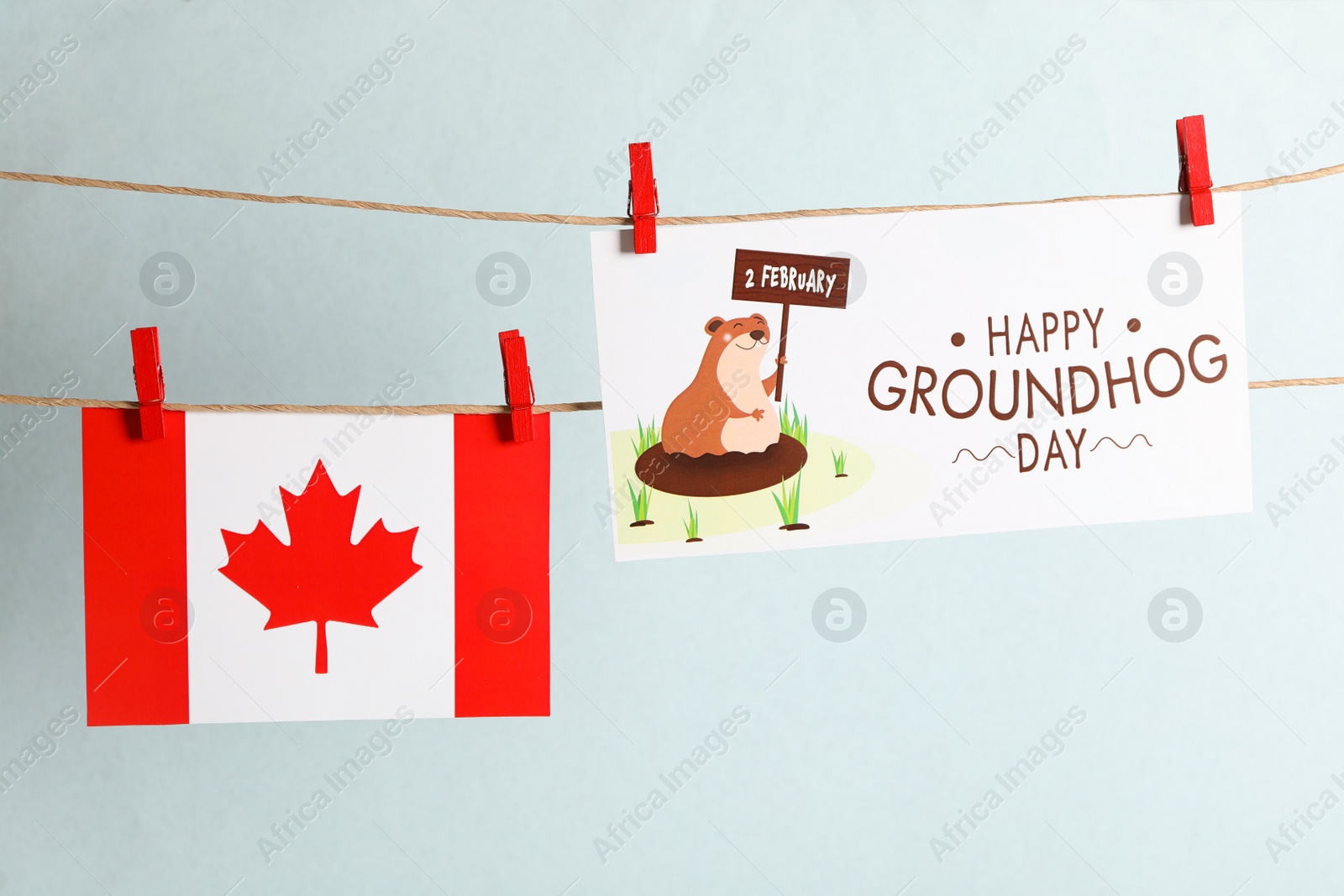 Photo of Happy Groundhog Day greeting card and Canada flag hanging against light background