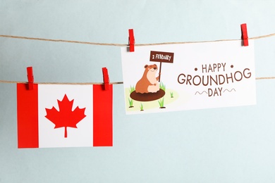 Photo of Happy Groundhog Day greeting card and Canada flag hanging against light background