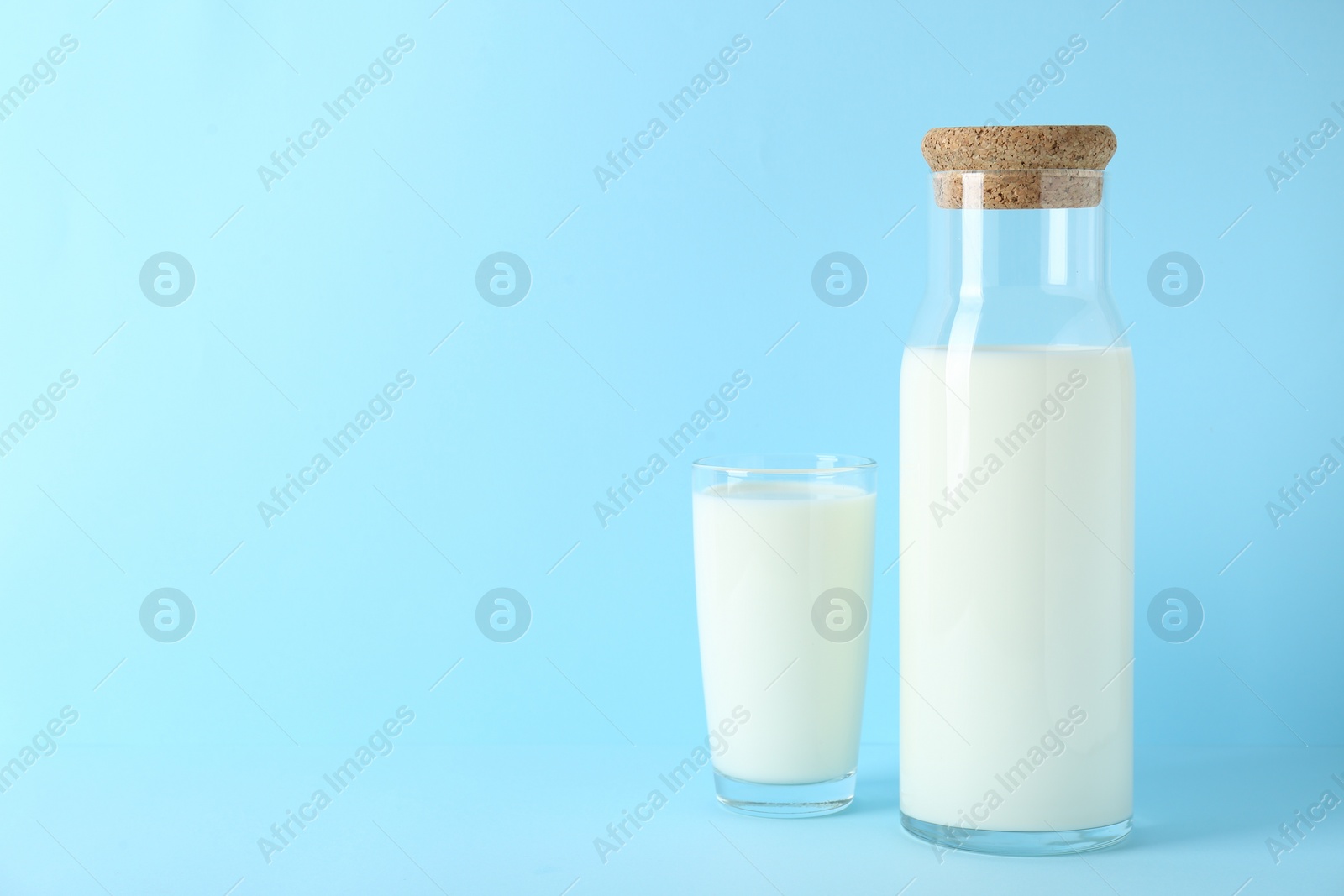 Photo of Carafe and glass of fresh milk on light blue background, space for text