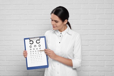 Ophthalmologist pointing at vision test chart near white brick wall