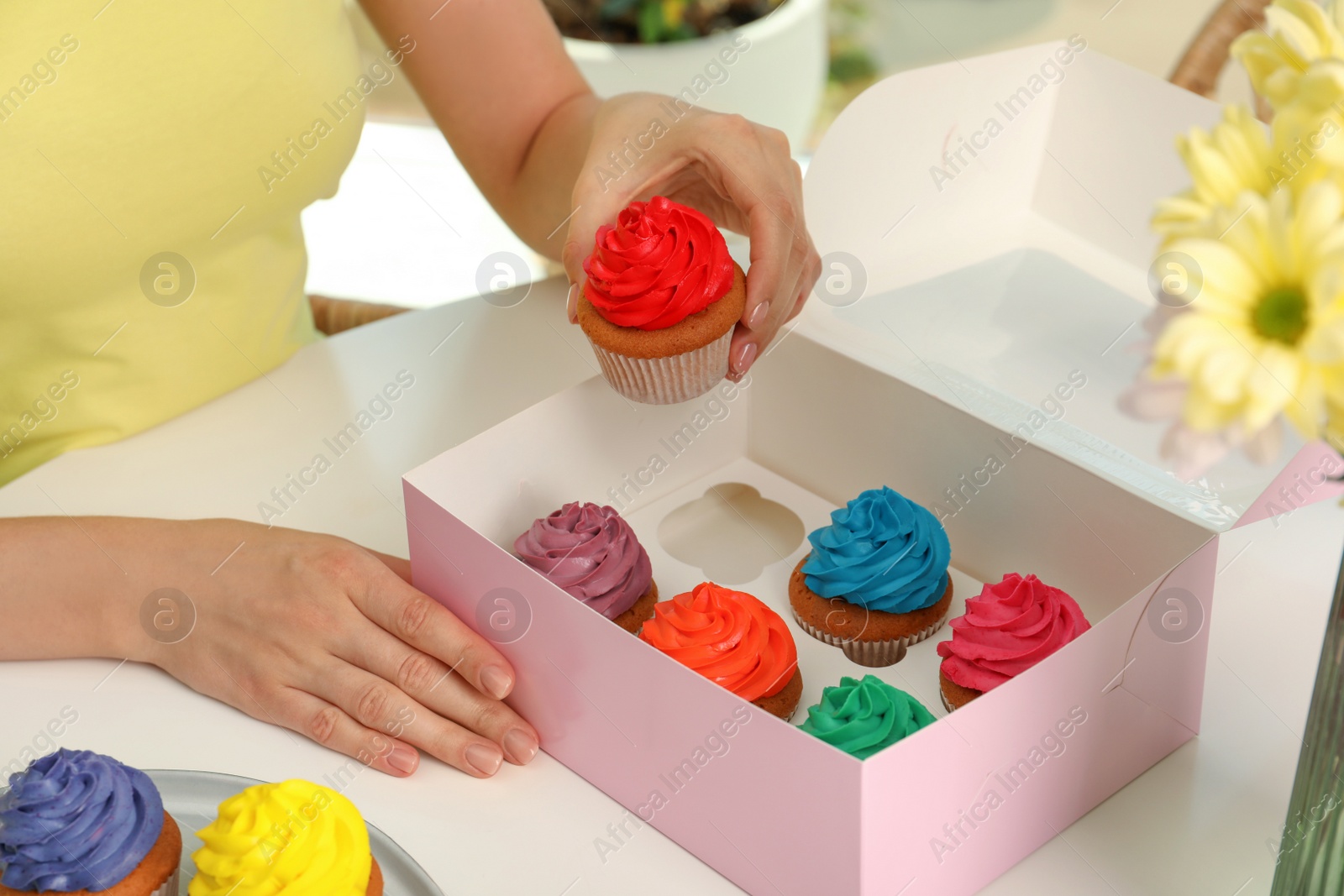 Photo of Woman with box of delicious colorful cupcakes at white table indoors, closeup