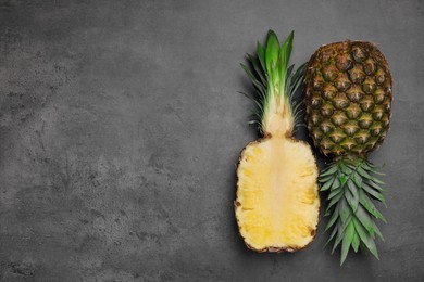 Whole and cut ripe pineapples on grey table, flat lay. Space for text