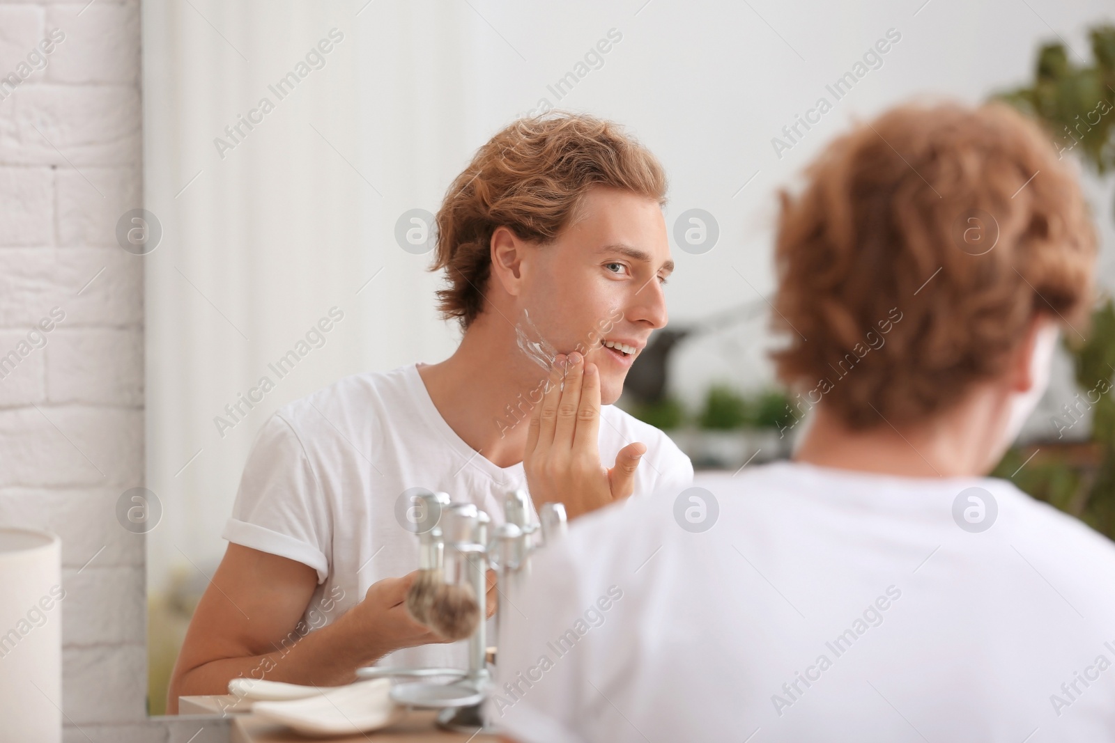 Photo of Young man applying shaving foam near mirror at home