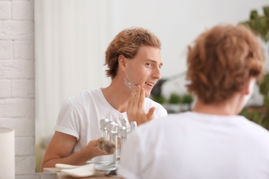 Young man applying shaving foam near mirror at home