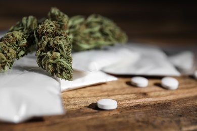 Photo of Cocaine, dried hemp and ecstasy on wooden table, closeup