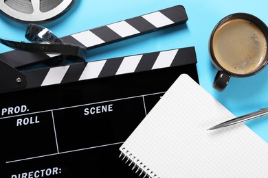 Photo of Movie clapper, film reel, coffee, notebook and pen on light blue background, flat lay