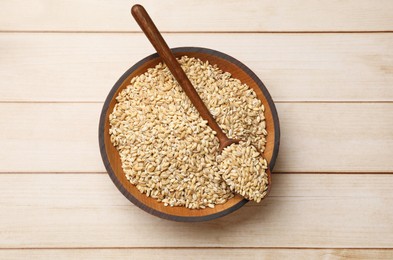 Dry pearl barley in bowl and spoon on light wooden table, top view