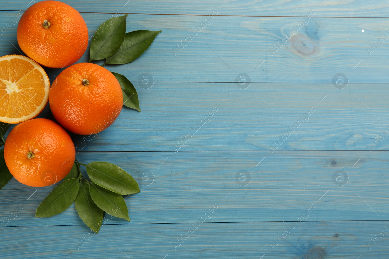 Photo of Delicious ripe oranges on light blue wooden table, flat lay. Space for text